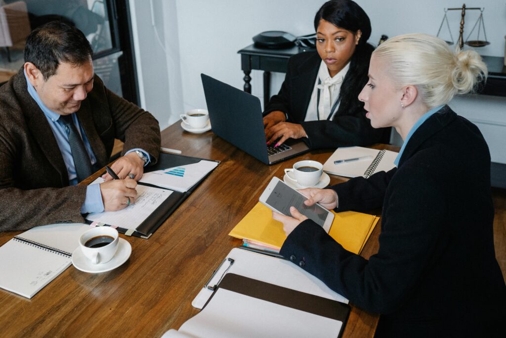 From above of multiracial colleagues in formal outfit working with papers laptop and tablet at table